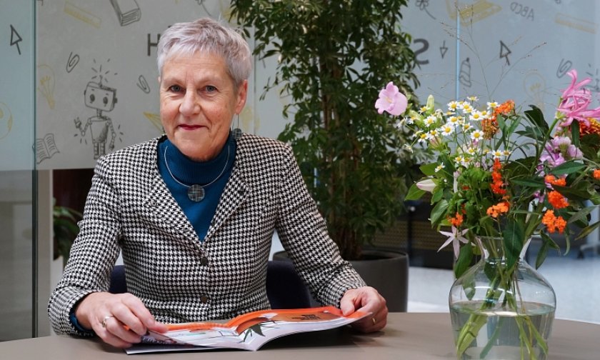 Een foto van SCOH-directeur Joke Snippe. Ze lacht vriendelijk, zit aan een tafel en heeft de Strategische Koers in haar handen. 